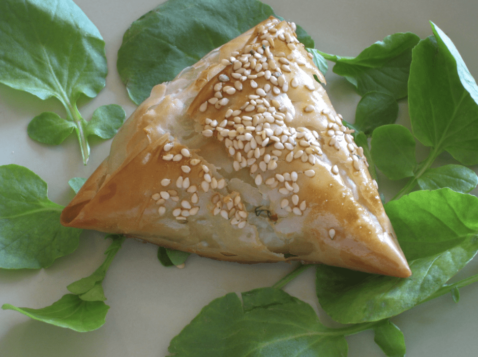 a triangle shaped pastry with sesame seeds on top of leaves